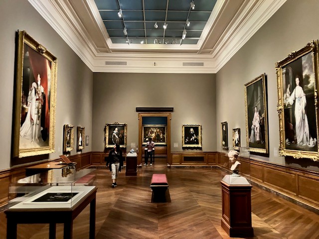 This image shows a museum gallery with several artworks on the walls and in the middle of the space
