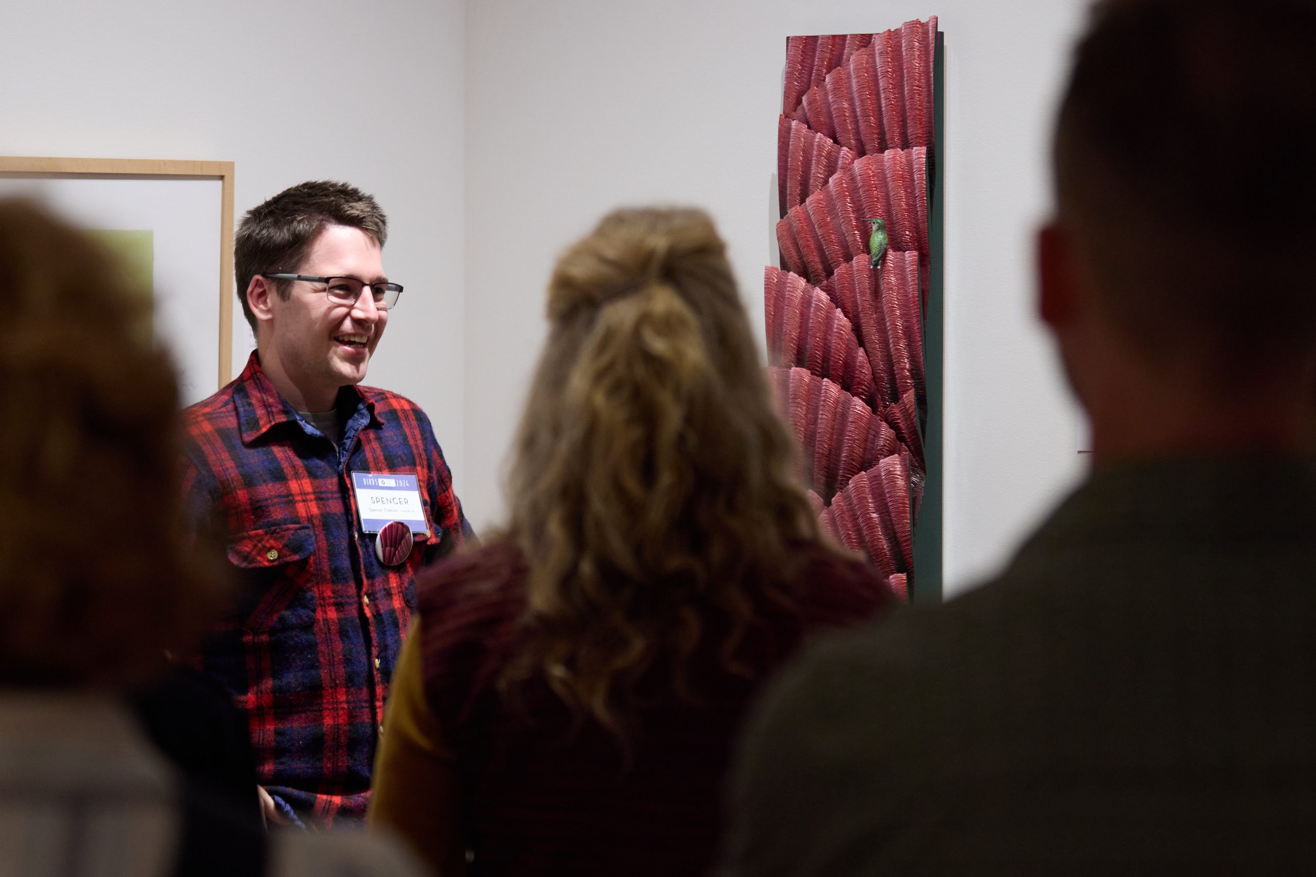 This image shows an artist smiling in front of his artwork talking to a crowd