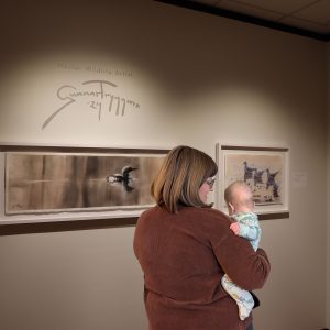 A woman stands with a baby in front of artworks