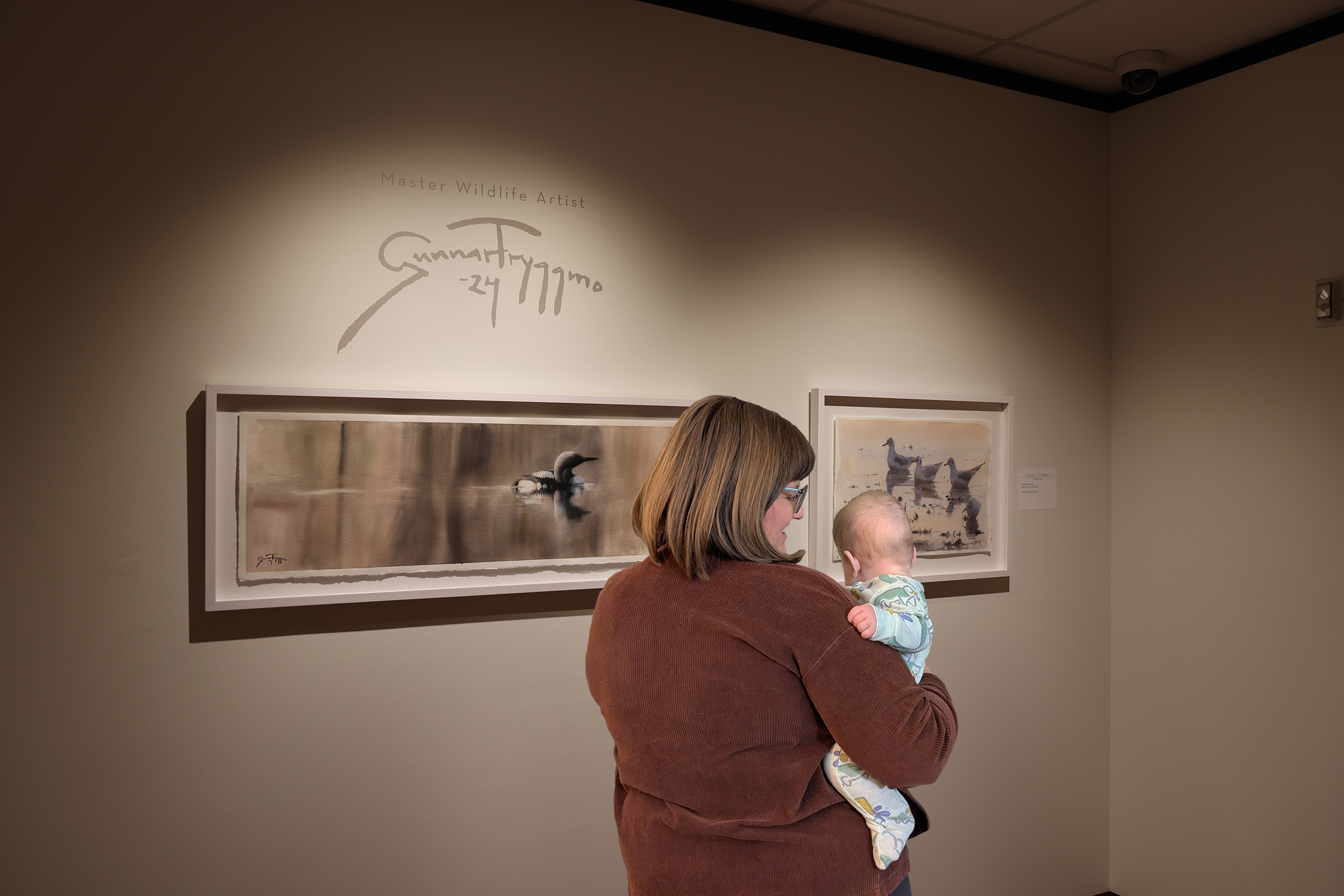 A woman stands with a baby in front of artworks