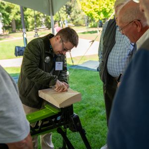 This image shows artist Spencer Tinkham carving a block of wood in front of four men watching him