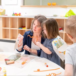 A mother and a child working together on an art project at a table in the Museum's classroom space.