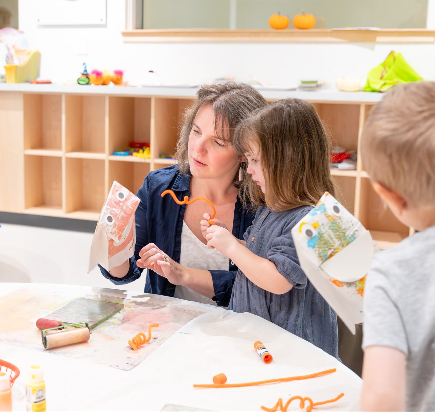 A mother and a child working together on an art project at a table in the Museum's classroom space.